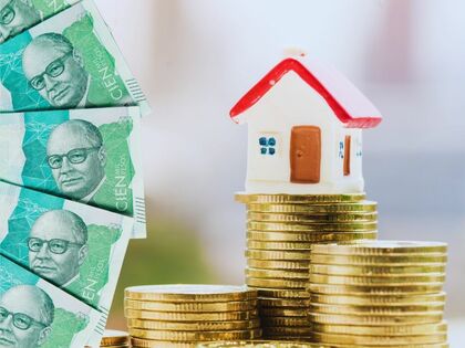 Imagen de una casa de juguete encima de monedas con billetes de 100 mil pesos