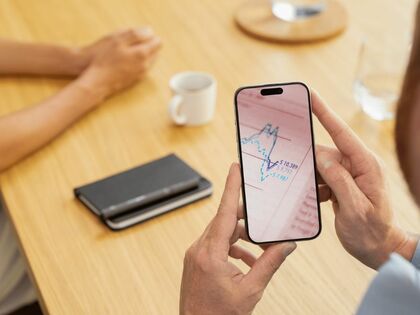 Mesa con moviles encima y una mano sosteniendo un móvil que muestra el desempeño de un fondo