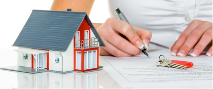 Persona firmando un contrato de vivienda con un llavero y una maqueta de casa sobre la mesa.