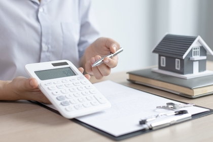 Persona calculando el precio de tasación de una vivienda con una calculadora y un contrato hipotecario sobre la mesa.