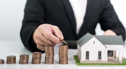 Hombre colocando monedas junto a una casa en miniatura, simbolizando la amortización de hipoteca y sus beneficios fiscales.