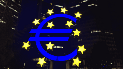 Símbolo gigante del euro rodeado de estrellas amarillas frente a varios edificios iluminados de noche, representando el contexto financiero europeo y la evolución del euríbor.