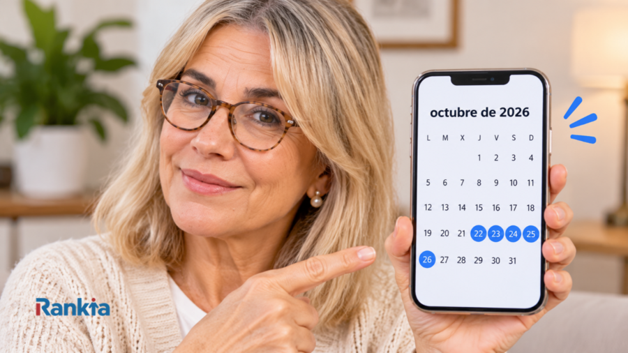 Mujer pensionista con gafas sonriendo y señalando un móvil con el calendario de octubre de 2026 en pantalla. Los días 22, 23, 24, 25 y 26 están marcados en azul porque son las fechas de cobro de la pensión en los distintos bancos. Logo de Rankia en la esquina inferior izquierda